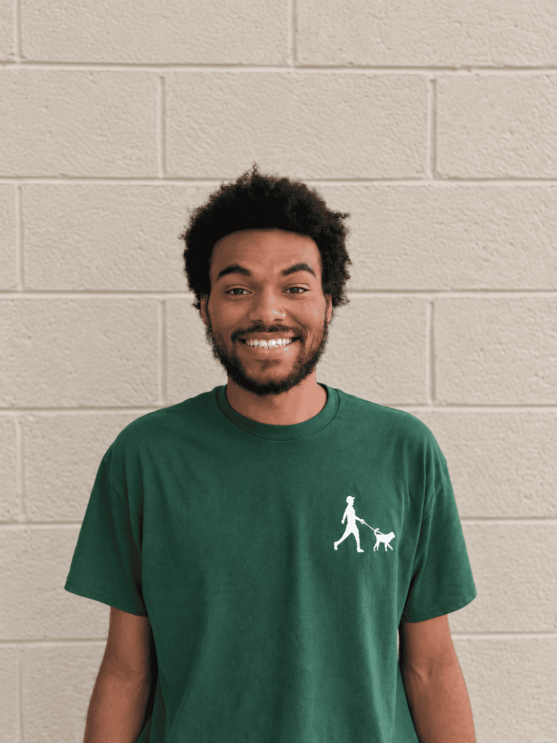Timothy Bright, Bethesda Dog Walkers team member, smiling in a green company shirt against a beige brick wall.